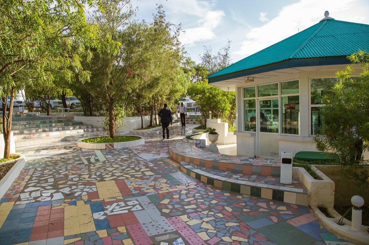 The garden at Ambassador Hotel Hargeisa: trees, a mosaic-tiled path and a pavilion with a green roof