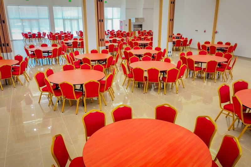 Ballroom set with round tables, with tall windows along the far wall