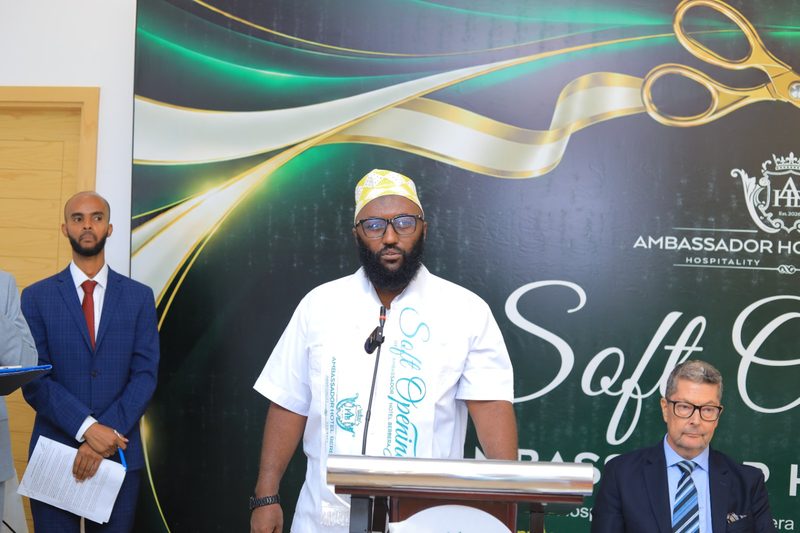 A speaker at the lectern in the Ballroom, in front of an Ambassador Hotel backdrop
