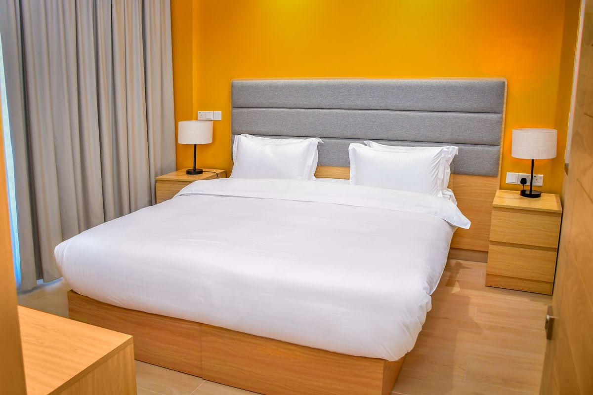 A Deluxe Room with a double bed, white linen and warm yellow walls